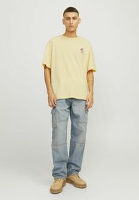 Gele katoenen t-shirt met korte mouwen, voorzien van een kleine afbeelding. Gecombineerd met blauwe cargobroek, die meerdere zakken en een ontspannen pasvorm heeft.