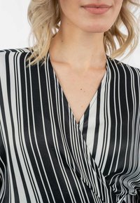 Blusa a rayas en blanco y negro con un diseño de cuello en V y textura de satén. Las rayas varían en grosor, aumentando el interés visual.