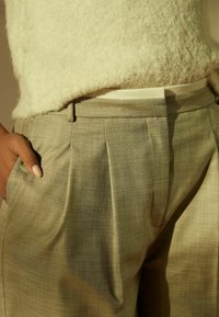 Grå plisserede bukser lavet af et struktureret stof, med en talje og sidelomme, parret med en fuzzy hvid sweater.
