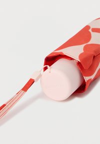 Κόκκινο και ροζ υφασμάτινο κάλυμμα με σχέδιο που στεγάζει έναν λευκό κυλινδρικό δοχείο με ροζ βάση, διαθέτοντας λουράκι και κούμπωμα που ταιριάζουν.