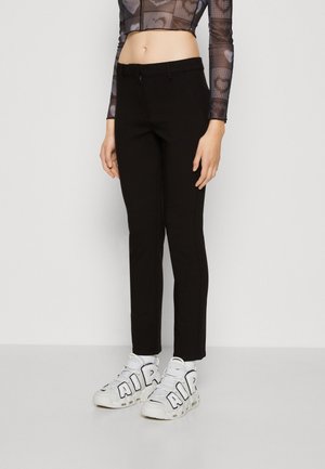 Personne portant un pantalon noir ajusté, des baskets blanches avec de grandes lettres "AIR" et un crop top en mesh à manches longues avec des motifs de cœur.