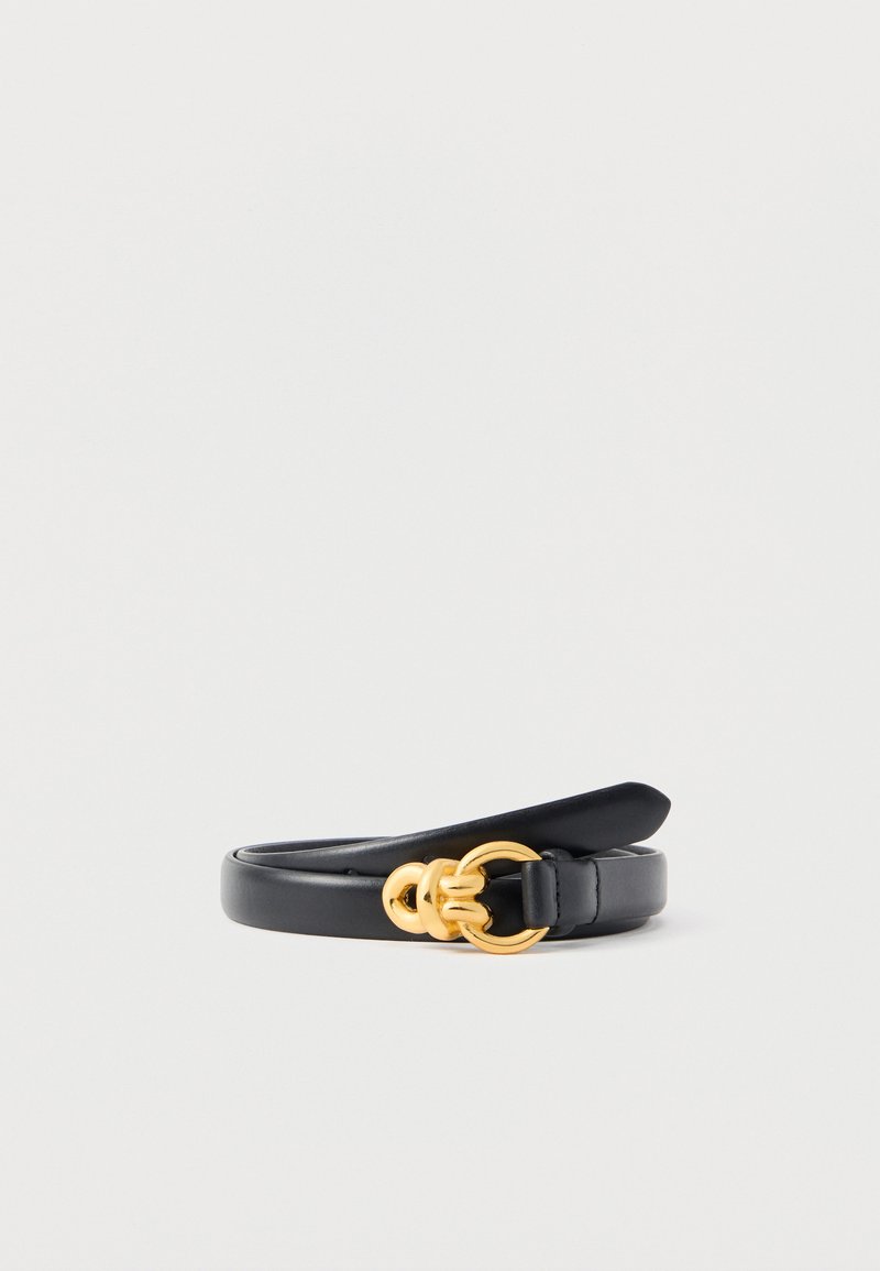 Ceinture en cuir noir avec une boucle circulaire dorée composée de deux anneaux liés, roulée et posée sur un fond blanc.