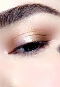 Close-up of an eye with shimmery bronze eyeshadow, dark lashes, and a soft peach-colored skin tone, highlighting the eyelid's texture and contour.