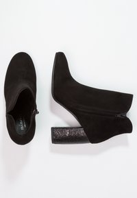 Czarne zamszowe botki za kostkę z teksturowanym czarnym obcasem w kształcie bloku oraz bocznym zamkiem błyskawicznym. Posiadają spiczasty czubek i gładką powierzchnię.