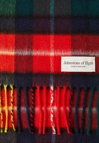 Wełniany szalik w kratę tartan w czerwono-zielono-granatowe wzory z frędzlami. Metka informuje "Johnstons of Elgin, wyprodukowano w Szkocji."
