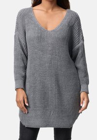 Pull gris en tricot avec un col en V profond, des manches longues et une coupe ample. Caractérisé par un tissu texturé et des poignets côtelés, atteignant le milieu des cuisses.