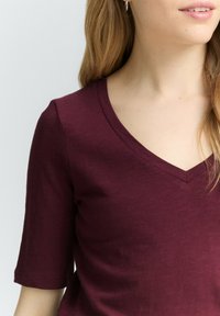 Bordeaux T-shirt met een V-hals en korte mouwen, gemaakt van zacht materiaal met een gladde textuur. Beschikt over een normale pasvorm en gestikte details.