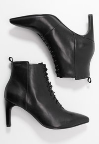 Botines de cuero negro que presentan una puntera puntiaguda, tacón alto, diseño de cordones y un acabado texturizado con una lengüeta en la parte trasera.