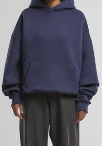 Sweat à capuche oversize bleu marine en tissu doux, doté d'une poche avant et d'une capuche réglable par cordon. Des poignets et un ourlet texturés complètent le design.