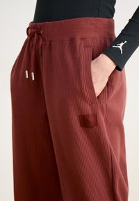 Bordeauxfarbene Jogginghosen mit einem strukturierten Waffelstrickdesign. Mit einem Kordelzugbund, Taschen und einem schwarzen Logopatch an der Seite.