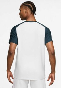 Camiseta deportiva para hombre con un cuerpo blanco y mangas raglán en verde azulado oscuro. Tejido suave, con mangas cortas y aberturas laterales en el dobladillo.