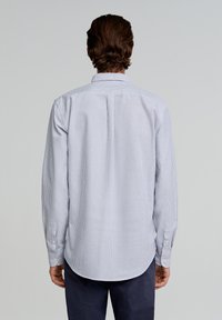 Gestreiftes Langarmhemd aus blauem und weißem Baumwollstoff. Mit klassischem Kragen und Knopfmanschetten sowie abgerundetem Saum. Die Rückansicht zeigt die Passform des Hemdes.