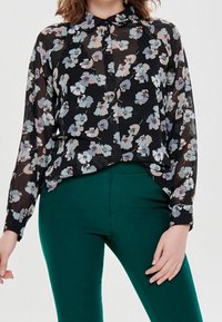 Czarna bluzka w kwiaty z długimi rękawami, zdobiona jasnoniebieskimi, różowymi i białymi wzorami kwiatowymi. Połączona z dopasowanymi zielonymi spodniami.