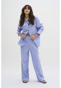 Cămașă cu carouri albastre deschise, dotată cu două buzunare pe piept, asociată cu o pereche de pantaloni largi asortați. Material neted, ușor. Stil casual.