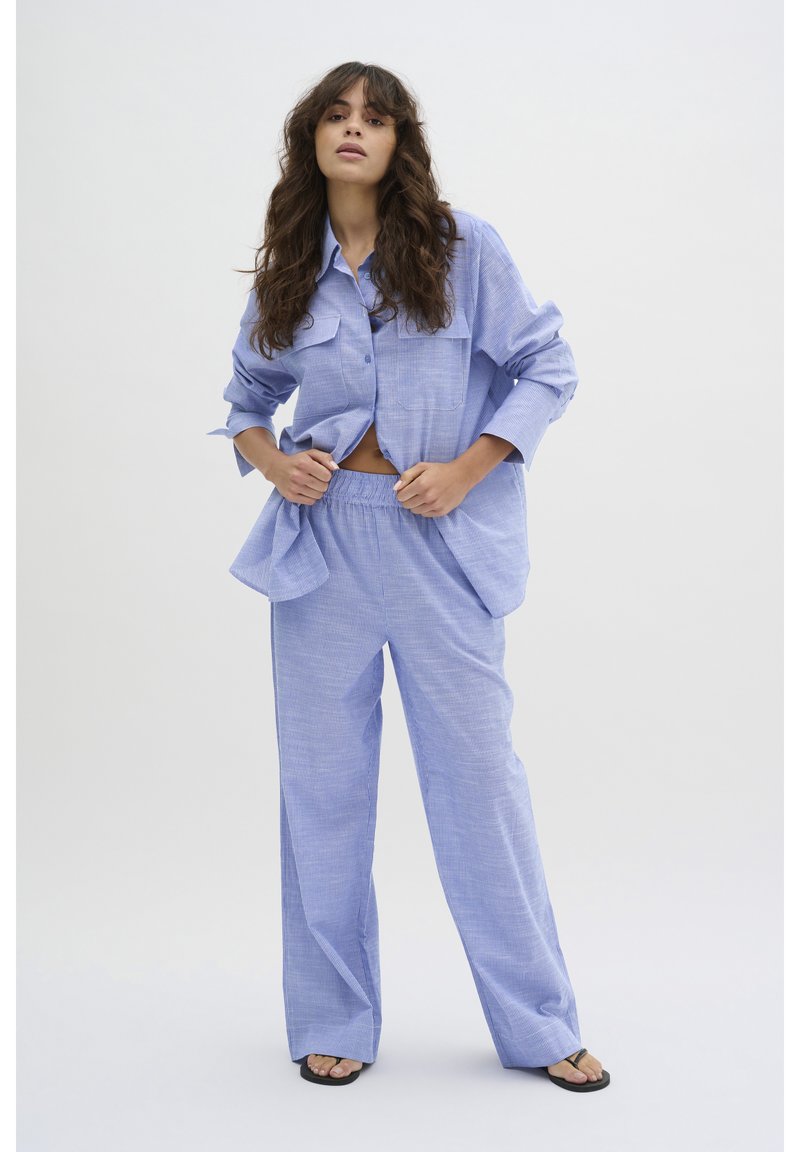 Cămașă cu carouri albastre deschise, dotată cu două buzunare pe piept, asociată cu o pereche de pantaloni largi asortați. Material neted, ușor. Stil casual.