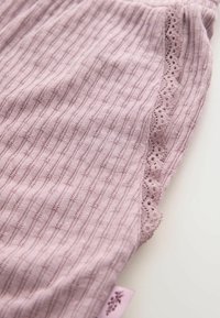 Tessuto rosa chiaro con una texture a coste e piccoli motivi in rilievo. Presenta un delicato bordo in pizzo su un lato e un piccolo etichetta.