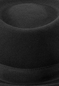 Fedora neagră din fetru, cu o coroană rotundă, textură netedă și o margine plată. Este decorată cu o bandă din grosgrain negru asortată la bază.