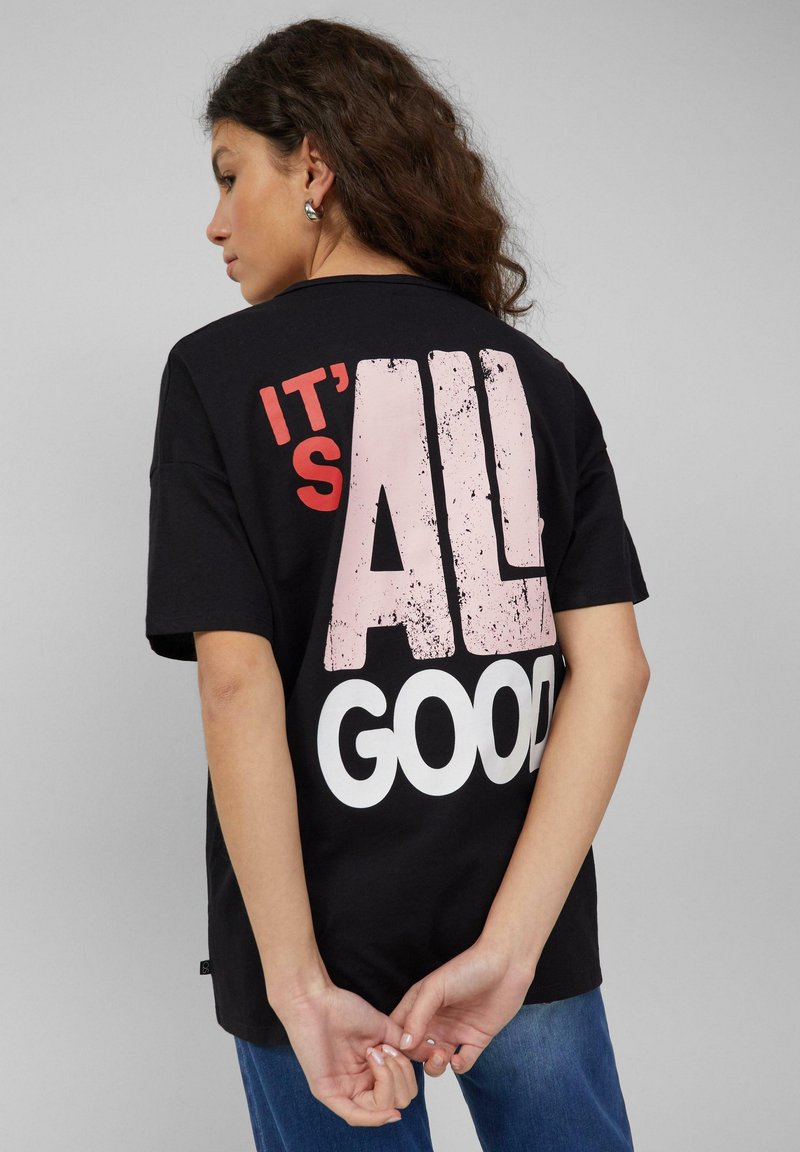 Zwart katoenen T-shirt met een grote, versleten grafische print in roze en wit op de achterkant met de tekst "IT'S ALL GOOD". Korte mouwen, losse pasvorm.