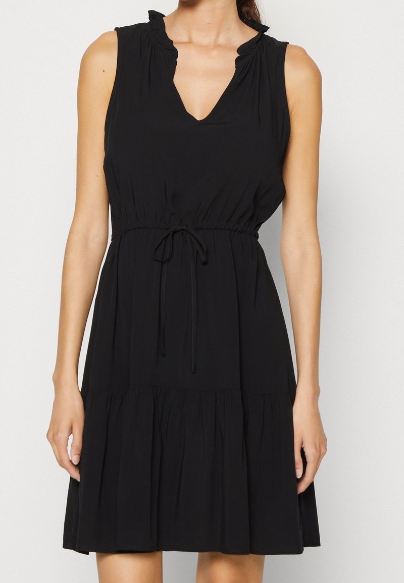 Svart ärmlös klänning med v-ringning, volangiga axlar, dragsko i midjan och en lager-på-lager kjol. Tillverkad av mjukt tyg med en slät yta.