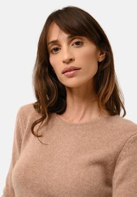 Helle beige gestrickte Pullover mit einem runden Ausschnitt und langen Ärmeln, der eine weiche Textur und ein dezentes, gleichmäßiges Muster aufweist.