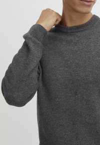 Grijze wollen crewneck trui met ribbelmanchetten en halslijn, een gladde textuur en een aansluitend ontwerp, weergegeven tegen een witte achtergrond.