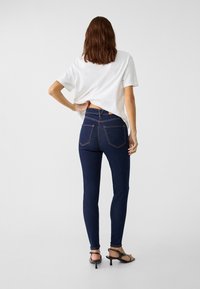 Skinny jeans in dark blue denim with back pockets, paired with a relaxed white t-shirt. The outfit features a minimalist design and clean lines.