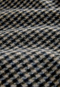 Gewebter Stoff mit einem Hahnentwist-Muster, das abwechselnd schwarze und tanfarbene Farben zeigt, mit einer weichen Textur und geschichteten Falten.