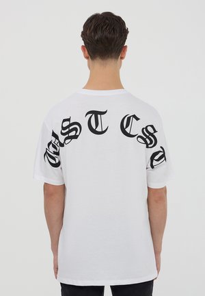 T-shirt bianco in cotone con grande lettering nero sul retro. Maniche corte, vestibilità rilassata, scollatura rotonda semplice, senza ulteriori motivi o dettagli.