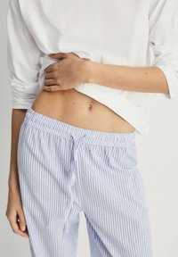 Striped pajama pants with blue and white vertical stripes, featuring an elastic waistband and drawstring detail. Soft, lightweight fabric.