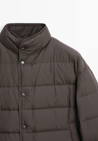 Giacca a vento imbottita marrone con colletto alto, caratterizzata da una texture trapuntata e bottoni a pressione lungo la parte anteriore per la chiusura.