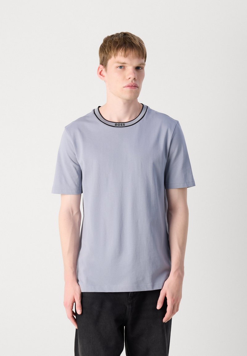T-shirt grigio chiaro a maniche corte con scollatura a girocollo, caratterizzato da un'etichetta nera "BOSS" sul colletto. Texture liscia e uniforme.