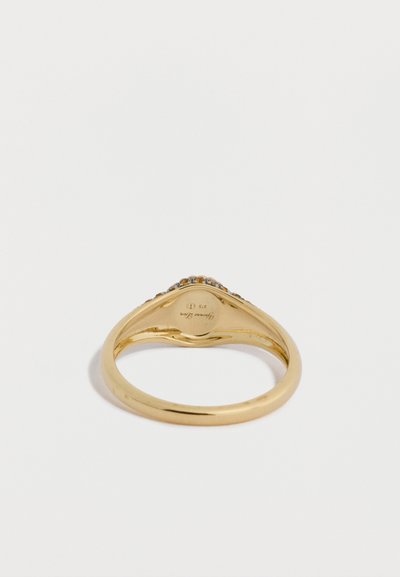 Zlatý prsteň s hladkým povrchom, na hornej hrane zapustený rad priehľadných kameňov. Vo vnútri je značený značkou a označením obsahu kovu.