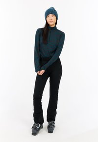 Conjunto de ropa de invierno en capas que incluye una camiseta de manga larga en color verde azulado con un patrón de olas, pantalones de esquí negros y botas de esquí grises.