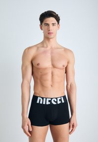 Boxer-briefs noirs avec un logo blanc "DIESEL" sur la ceinture, fabriqués en tissu lisse, avec une coupe ajustée et une longueur mi-cuisse.