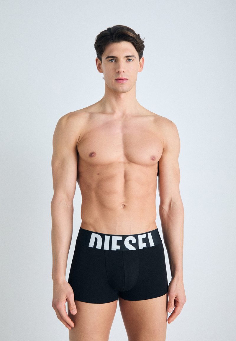 Boxer-briefs noirs avec un logo blanc "DIESEL" sur la ceinture, fabriqués en tissu lisse, avec une coupe ajustée et une longueur mi-cuisse.
