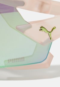 Lunettes de soleil avec une monture rose translucide, des lentilles dégradées vertes, un logo Puma bien visible et un design géométrique avec des bords anguleux.