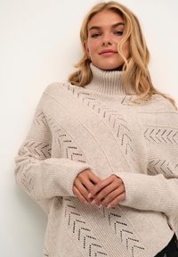 Beige pletený svetr s vysokým rolákem, zdobený vzorem do V a manžetami s žebrováním, vyrobený z měkké, texturované látky.