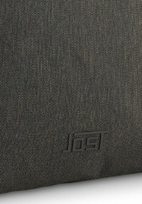 Bolso de tela gris con una superficie texturizada, un patrón sutil y un logotipo en relieve en la esquina inferior derecha.