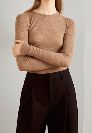Haut à manches longues et col rond en marron clair, fabriqué à partir d'un tissu doux et texturé. Porté avec un pantalon noir taille haute, créant une silhouette élégante.