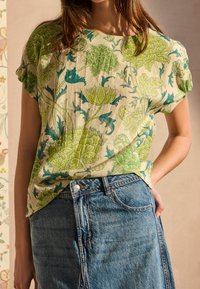 Bluse med blomstermønster i grøn og blå på en lys baggrund, lavet af letvægtsstof. Kombineret med en højtaljet denimnederdel.