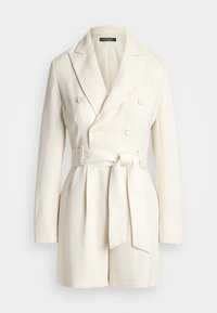 Διπλής όψης κρεμ ζακέτα με ζώνη στη μέση, σατινέ υφή, αιχμηρές πατιλέτες και μπροστινές τσέπες. Τα κουμπιά είναι κρεμ με λεία επιφάνεια.