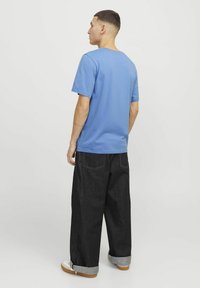 Lyseblå bomulds t-shirt med rund hals, kombineret med mørke denim bukser med vidde og opsmøg ved buksebenene samt synlige sømme.