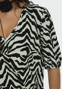 Černobílý top se zebra pruhy s texturovaným skládaným designem, s hlubokým výstřihem do V a krátkými nařasenými rukávy.