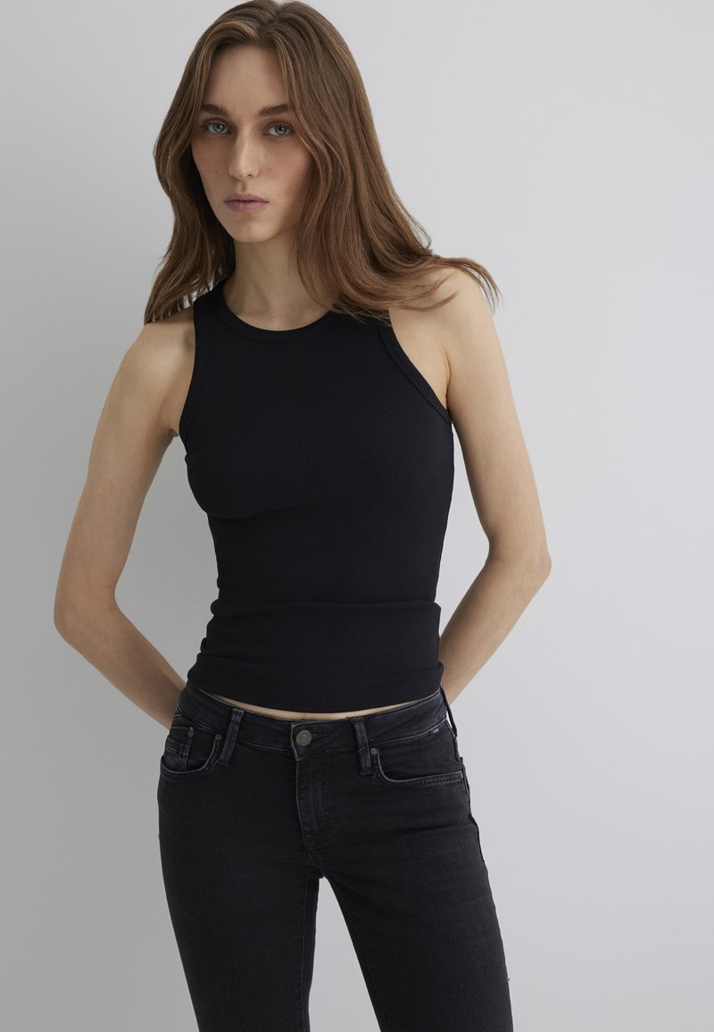Black ribbed tank top with a fitted design and sleeveless cut, paired with dark denim jeans featuring front pockets and a button closure.