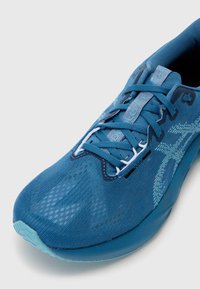 Chaussure de sport bleu avec tige en mesh texturé, embout renforcé et lacets blancs contrastants. Dispose d'une semelle rembourrée et de détails de logo subtils.