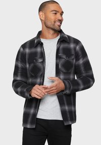 Schwarz-weiß karierter Flanellhemd mit einem Kragen, zwei Brusttaschen mit Knopfverschluss und Knopfmanschetten. Weicher Stoff.