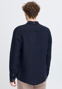 Camicia a maniche lunghe blu navy in tessuto di lino, con colletto button-down e bottoni ai polsini, caratterizzata da una spalla posteriore dritta e fessure laterali.