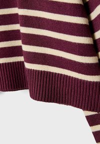 Gros plan sur un tissu tricoté avec des rayures horizontales crème et rouge foncé et un ourlet côtelé rouge foncé.