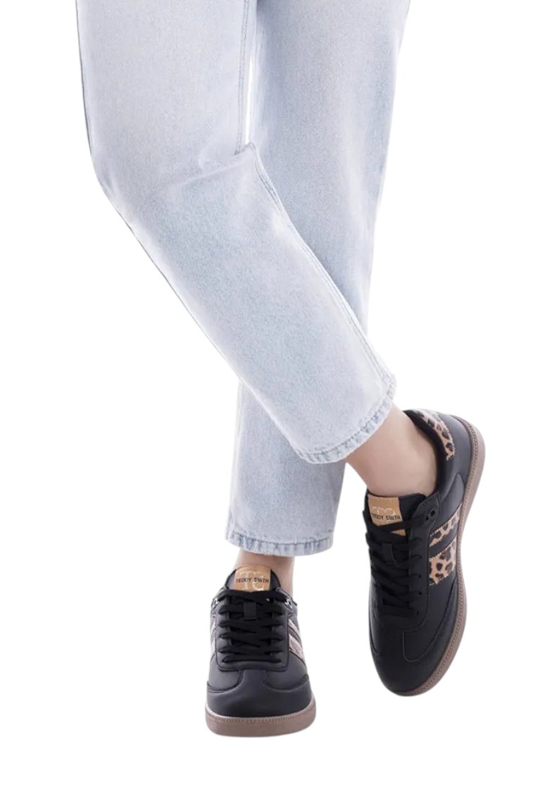 Baskets noires avec des accents en imprimé léopard et des semelles en caoutchouc marron, associées à un jean cropped bleu clair. Lacets et matériau texturé visibles.