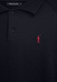 Schwarzes Polo Club-Shirt mit geripptem Kragen, zwei Knöpfen und kleinem, roten, gesticktem Polo-Spieler-Logo auf der Brust.